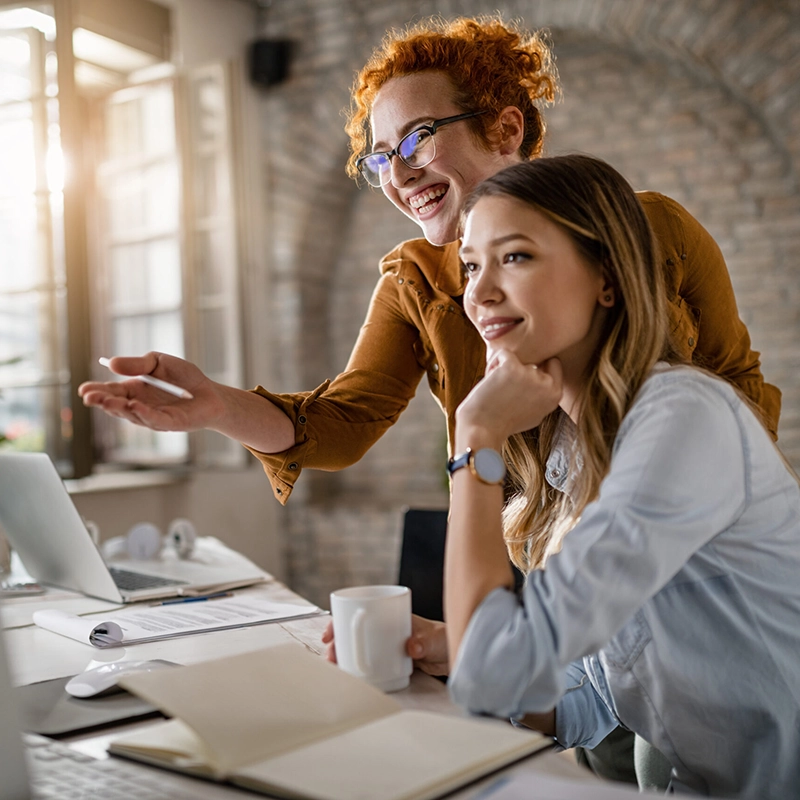 Happy female entrepreneurs reading an e-mail on computer while working together in the office. Focus is on redhead woman.